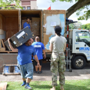 Service member oversees movers unpacking her personal belongings from moving truck.