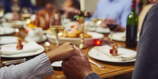Family holds hands around dinner table.