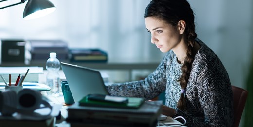 A young woman sits at a desk and uses a laptop computer.