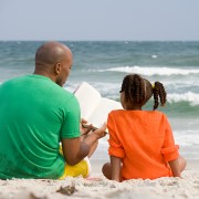 Father reading with daughter on beach.