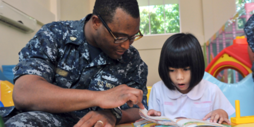An airman reads with a little girl.