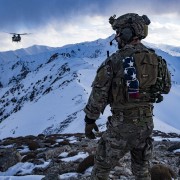 Service member looks over mountains as helicopter approaches.