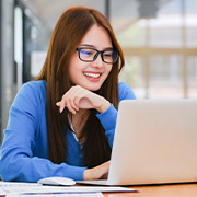 Woman in blue smiling at laptop.