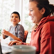 Mother using laptop and laughing with son with special needs.