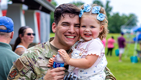 Service member father smiles and holds their daughter.