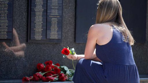 Woman holding rose looking at memorial