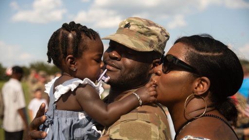 service member and spouse embracing toddler