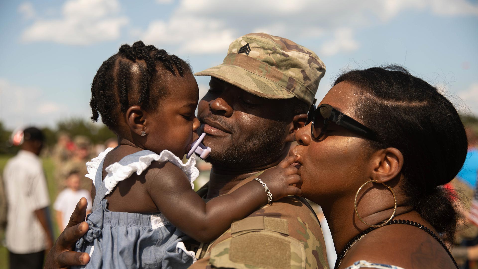 service member and spouse embracing toddler