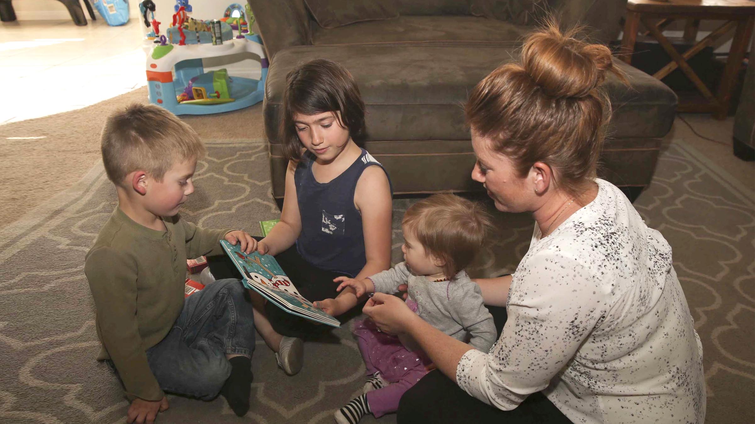 Mother and her children reading a book in the living room.