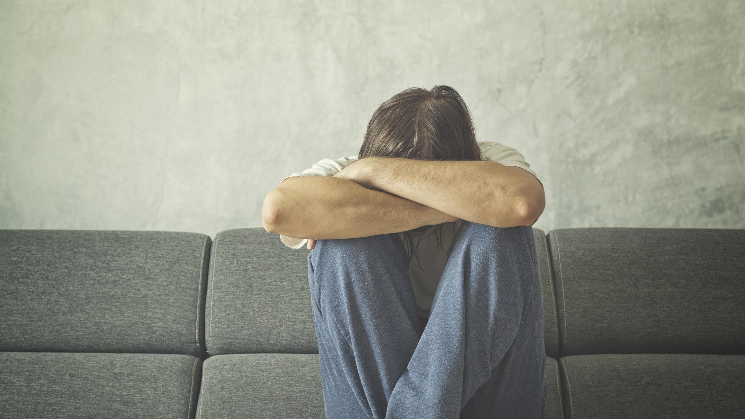 Man on couch with head in arms