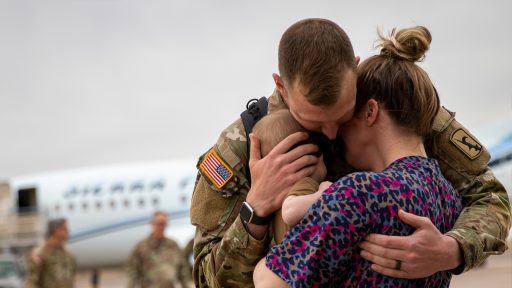 Service member hugging spouse and baby