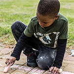 Young boy draws on ground with chalk