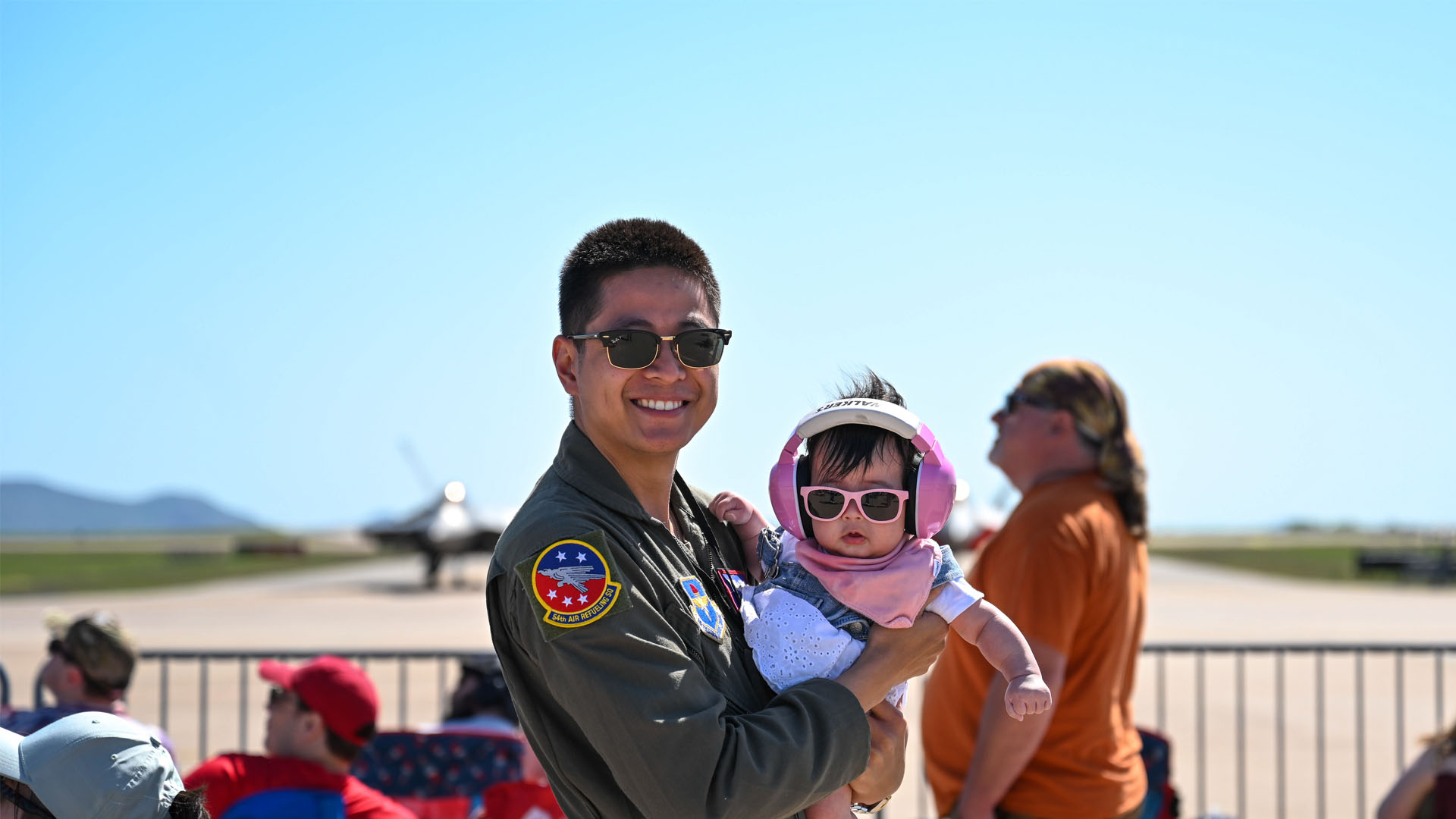 Service member holding child wearing sunglasses