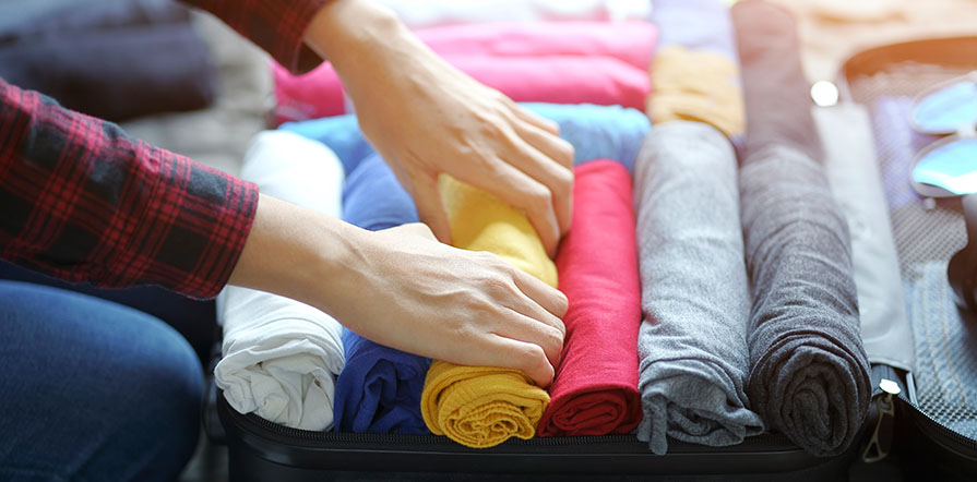 woman hand packs clothes in suitcase on bed
